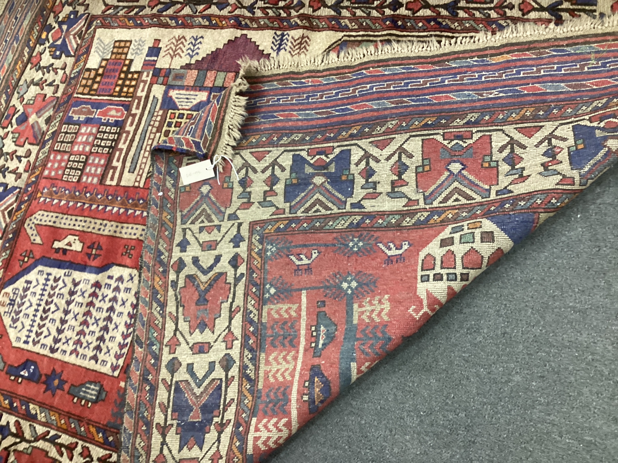 A mid 20th century Afghan red ground pictorial rug woven with an abstract city scene, 180cm x 140cm.